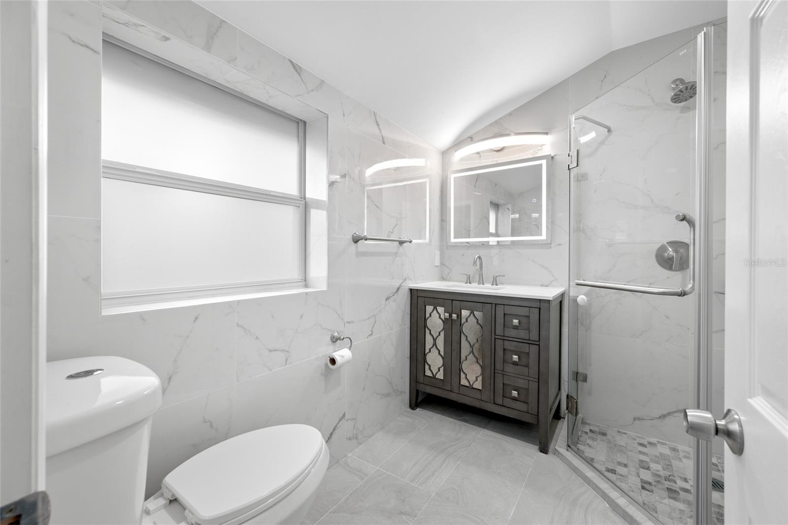 Primary Bedroom suite with walk-in closet, with built in shevles, that opens through to private en-suite updated bathroom with marble tile and glass shower.