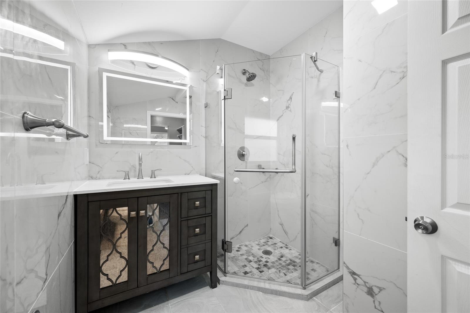 Primary Bedroom suite with walk-in closet, with built in shevles, that opens through to private en-suite updated bathroom with marble tile and glass shower.