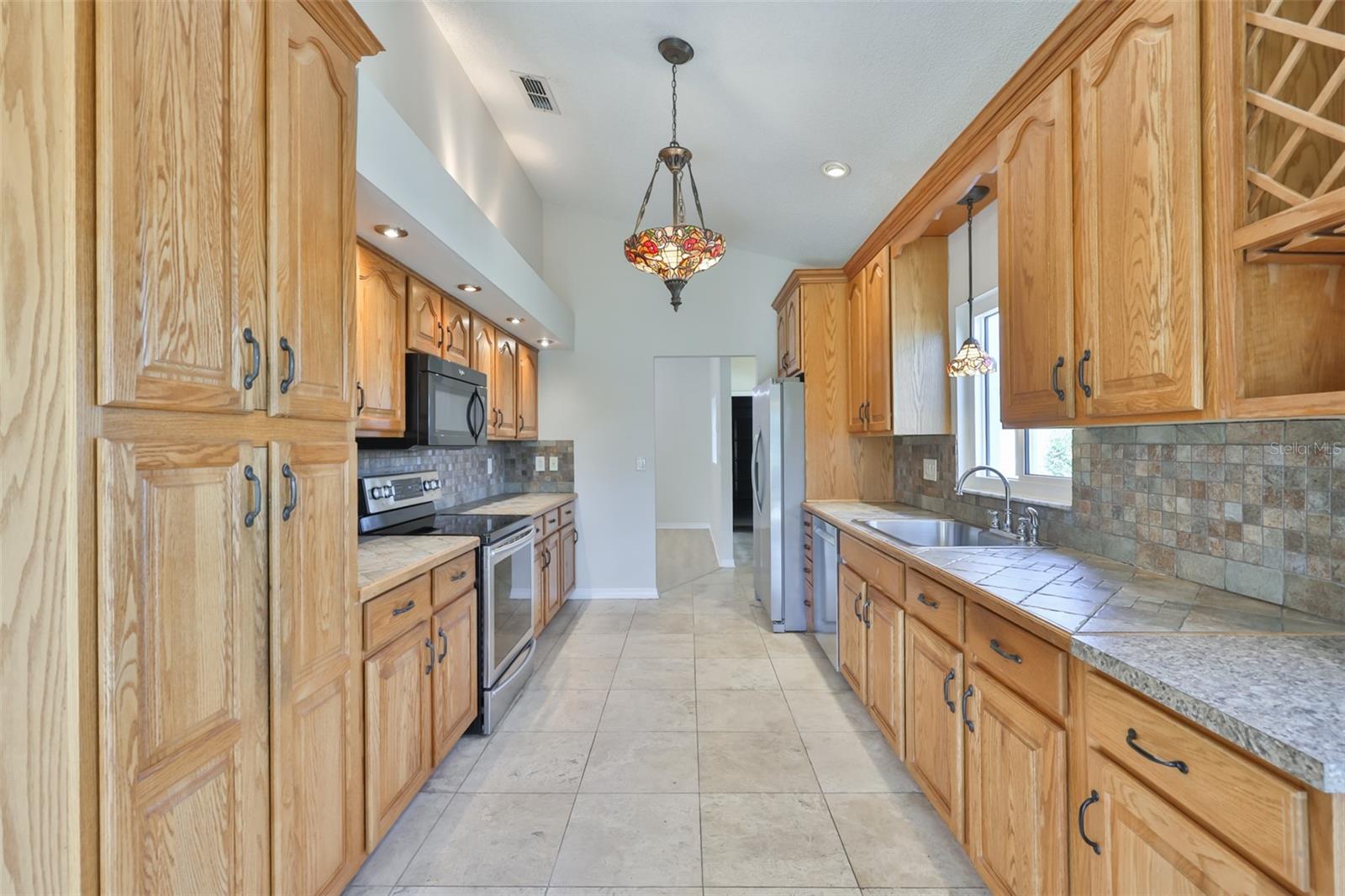 Galley Kitchen with all wood cabinets, wine rack, tile counters and backsplash.