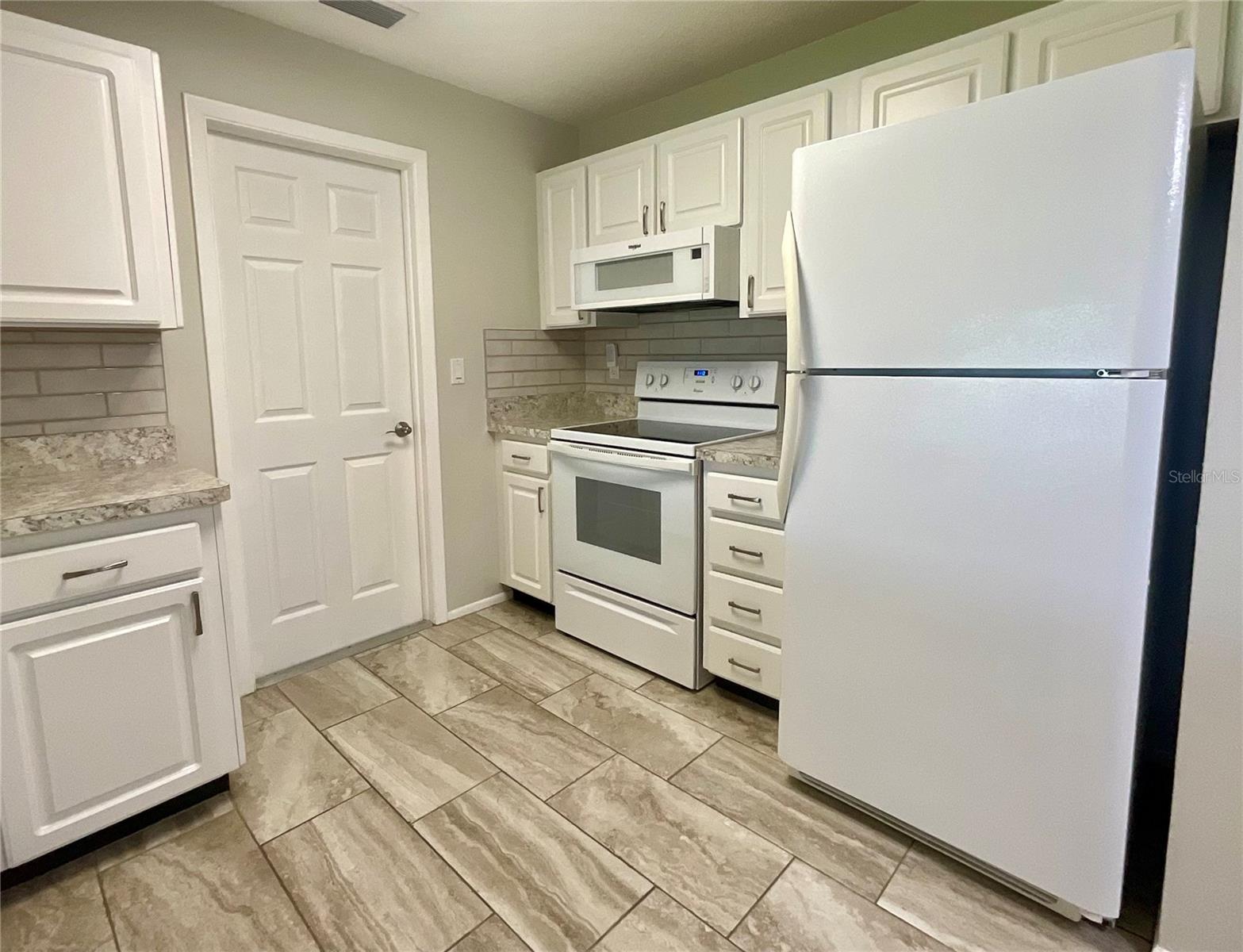 Kitchen range, refrigerator, microwave area and door to garage laundry area