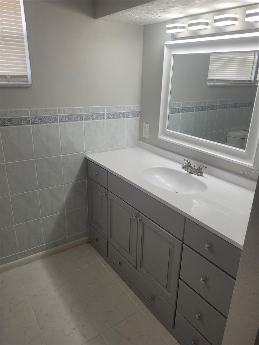 primary bathroom suite remodeled with new vanity with quartz countertops, new tile, new floors, lighting, & hardware