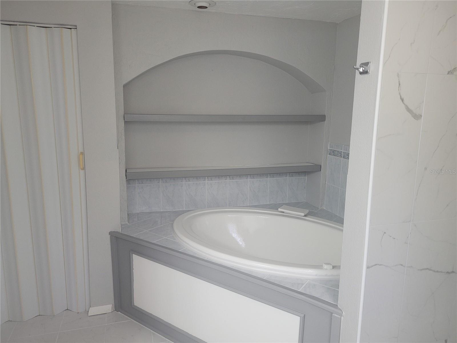 primary bathroom with Jacuzzi tub, shelves, and a closet