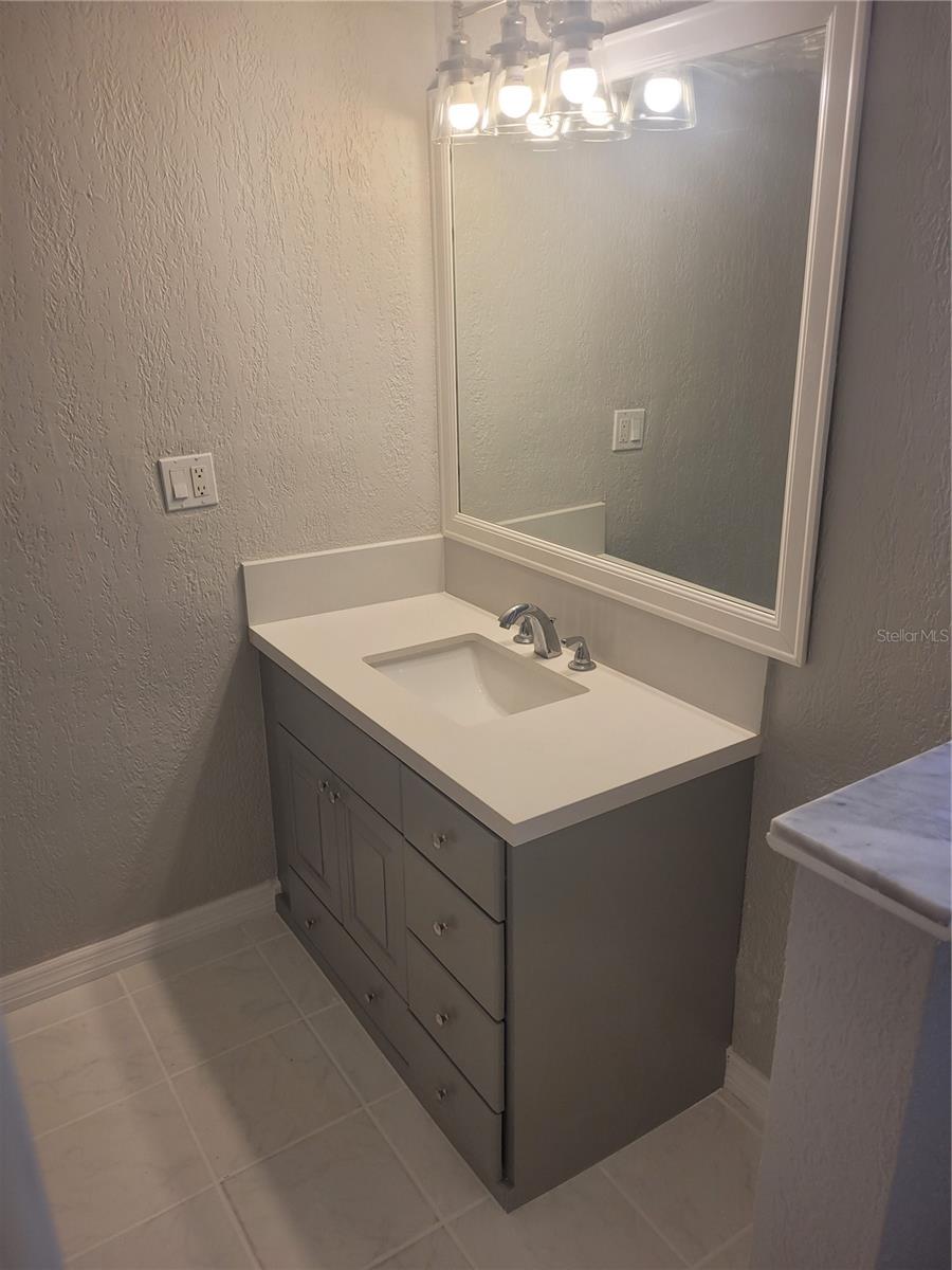 remodeled guest bathroom with new floors, vanity with quartz countertops, toilet, tile, and hardware