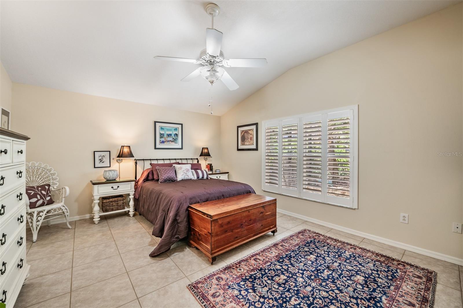 Master Bedroom with Plantation Shutters,  Two Closets, Tile Flooring and a ceiling fan with a light fixture.