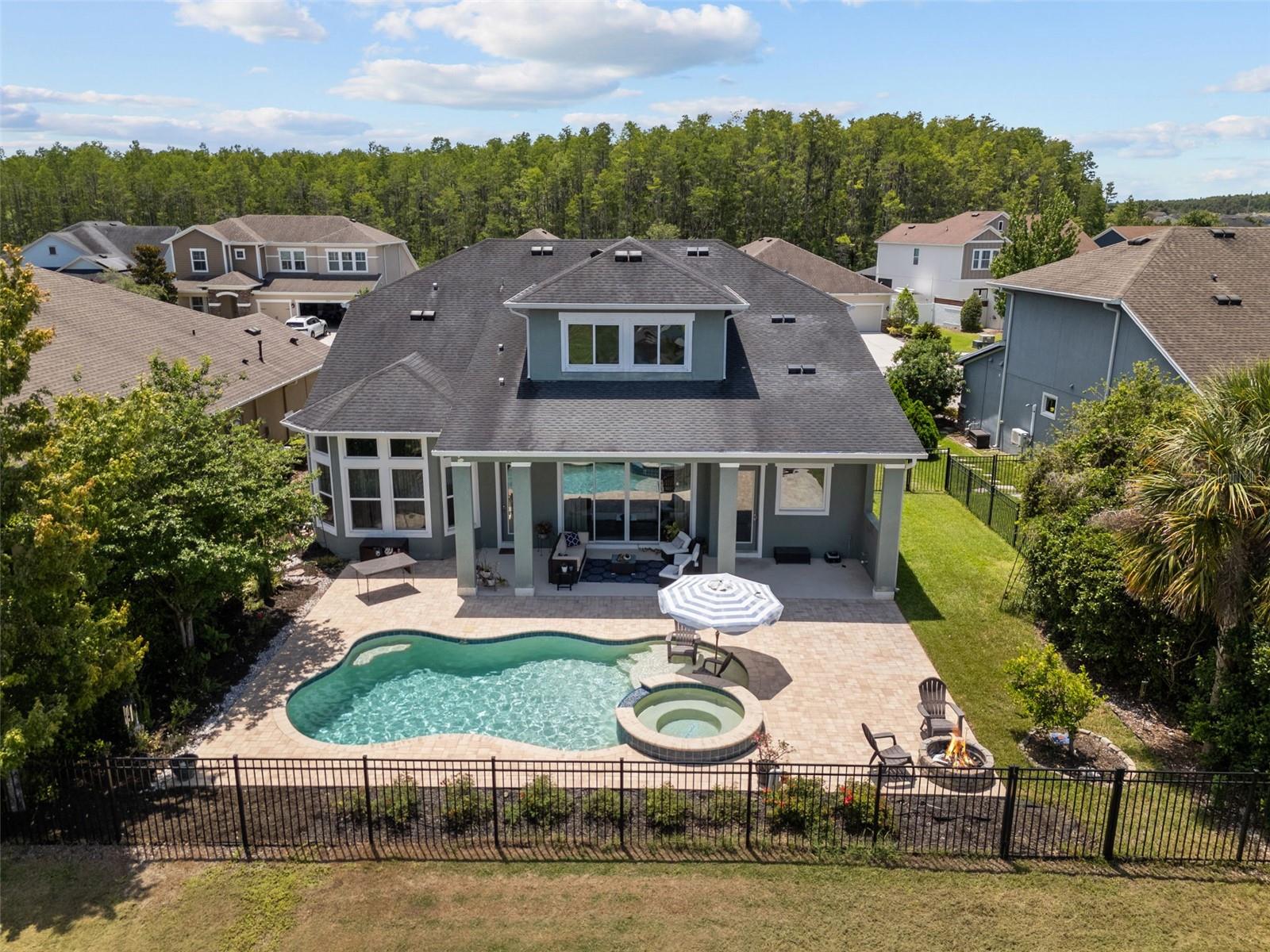 Rear aerial view highlighting the private pool, spa, paver patio, and pond-view backyard.