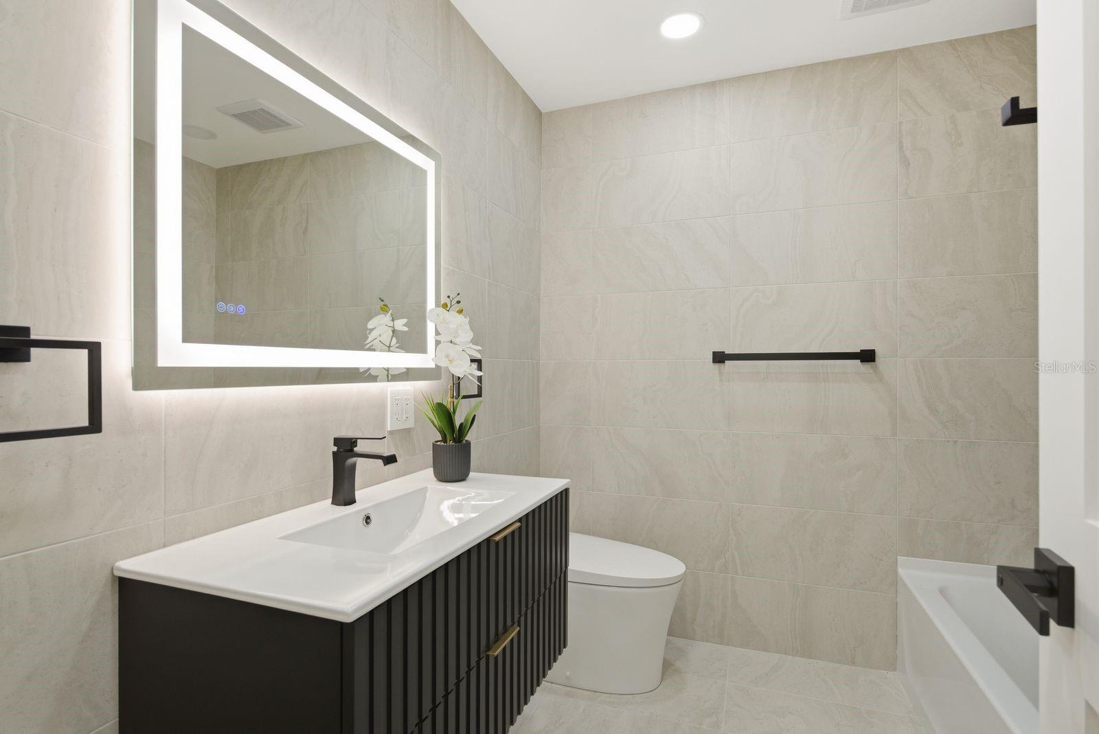 Bathroom #2 featuring a bath tub, modern vanity, toilet/bidet combo and a mirror with light