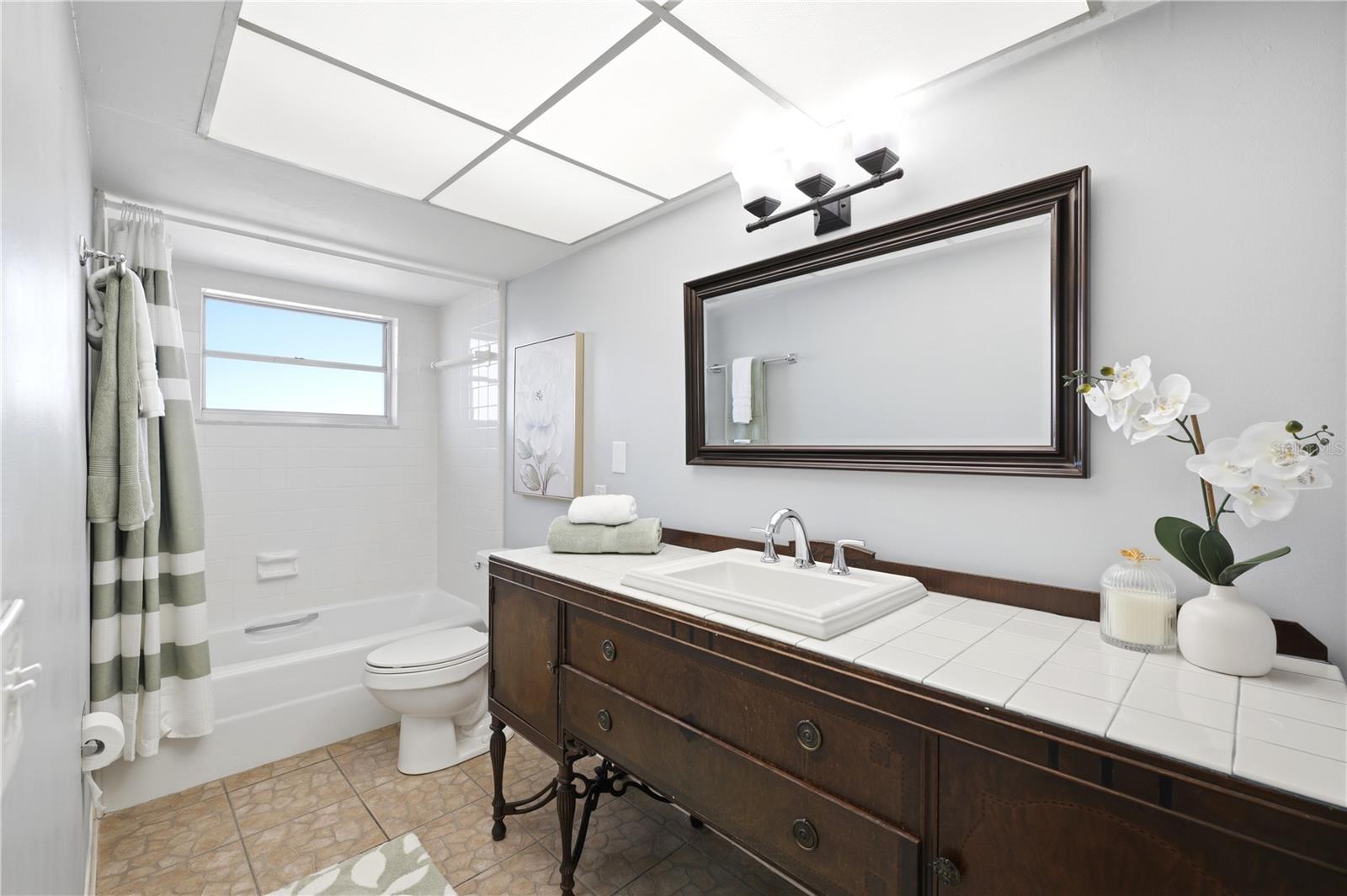 shared guest bathroom with second bedroom with a vintage vanity and tub/shower combination
