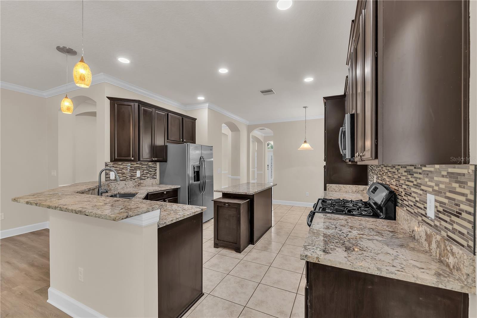 The gourmet kitchen is equipped with stainless steel appliances, rich wood cabinetry, granite countertops, mosaic tile backsplash, breakfast bar, center island, and Buyers will love cooking with a Gas Range!