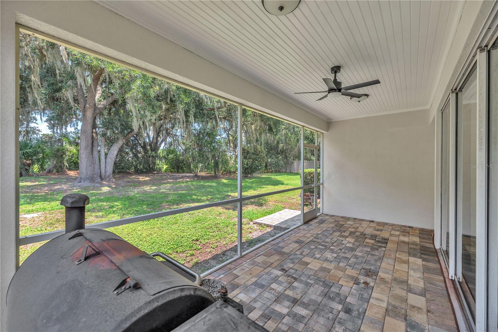 Step outside to the screened lanai featuring stone pavers and a wood-paneled ceiling — the perfect place to relax and enjoy the peaceful backyard with no rear neighbors.