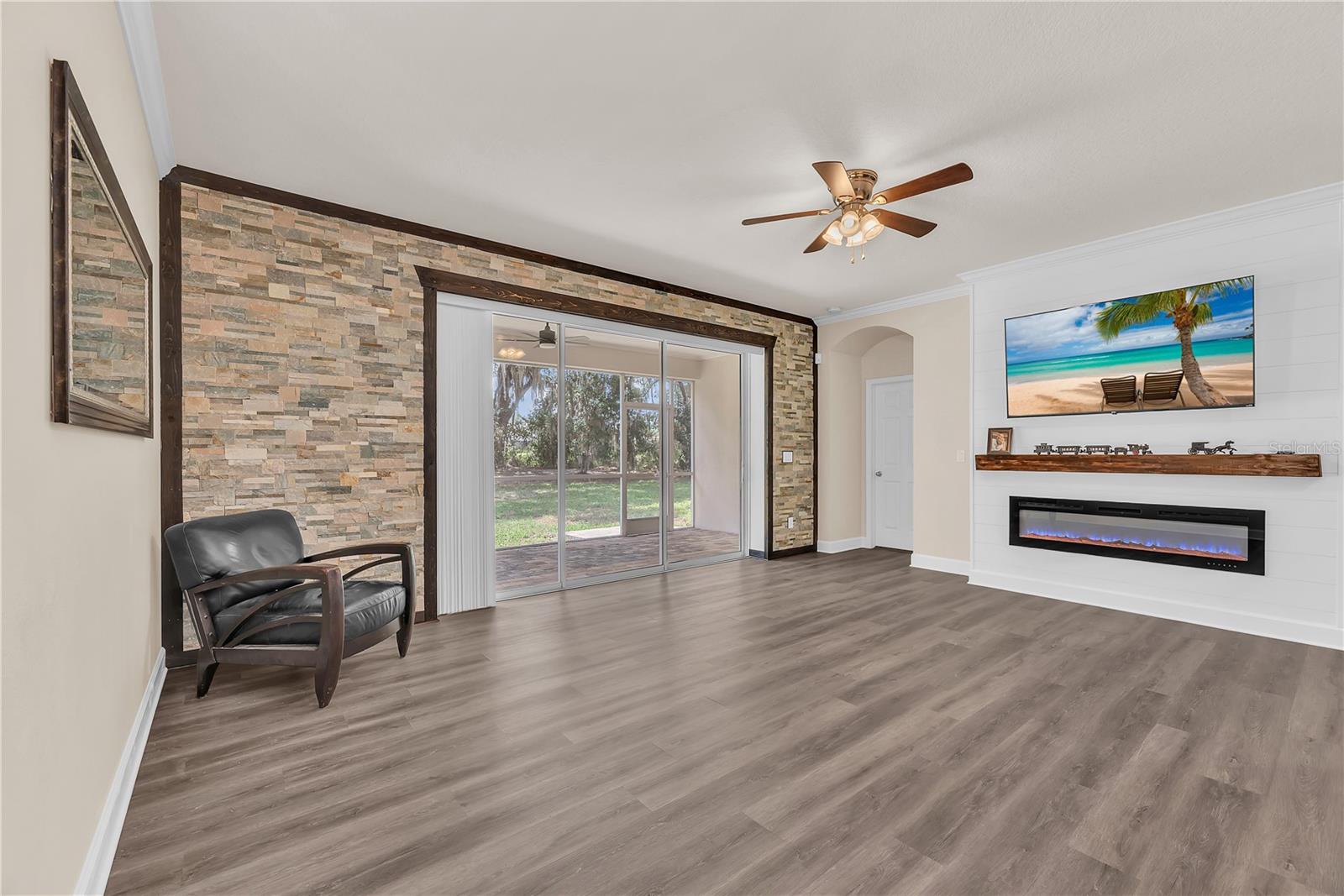 The family room showcases a beautiful electric fireplace set against a stylish shiplap accent wall, while a stone feature wall surrounding the triple sliding glass doors adds warmth and rustic charm.