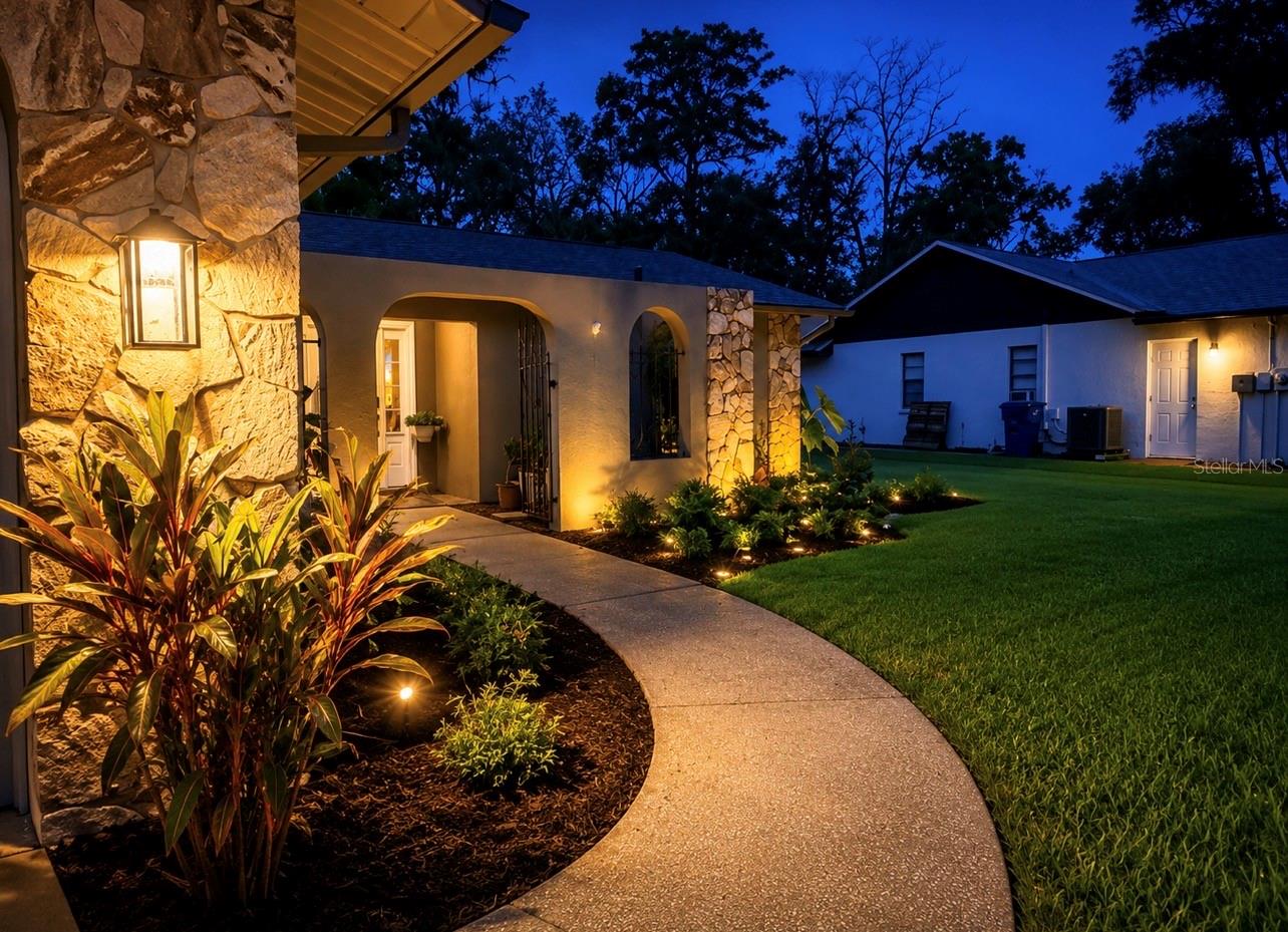 HOME SURROUNDED WITH EXTERIOR LIGHTING AND LUSH LANDSCAPING