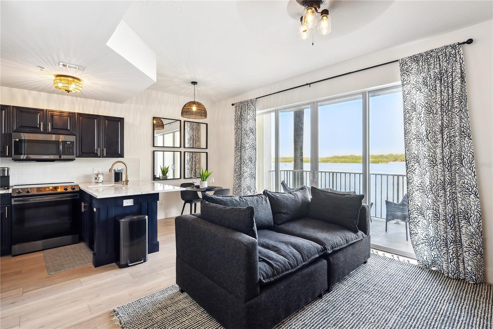 View of Living room, kitchen with Cambria Quartz "Portrush" series luxury countertops, dining room, oversized hurricane-rated tinted sliders leading to the balcony with luxury vinyl flooring throughout, Leather pull-out sleeper sofa and custom blackout temperature reducing drapes