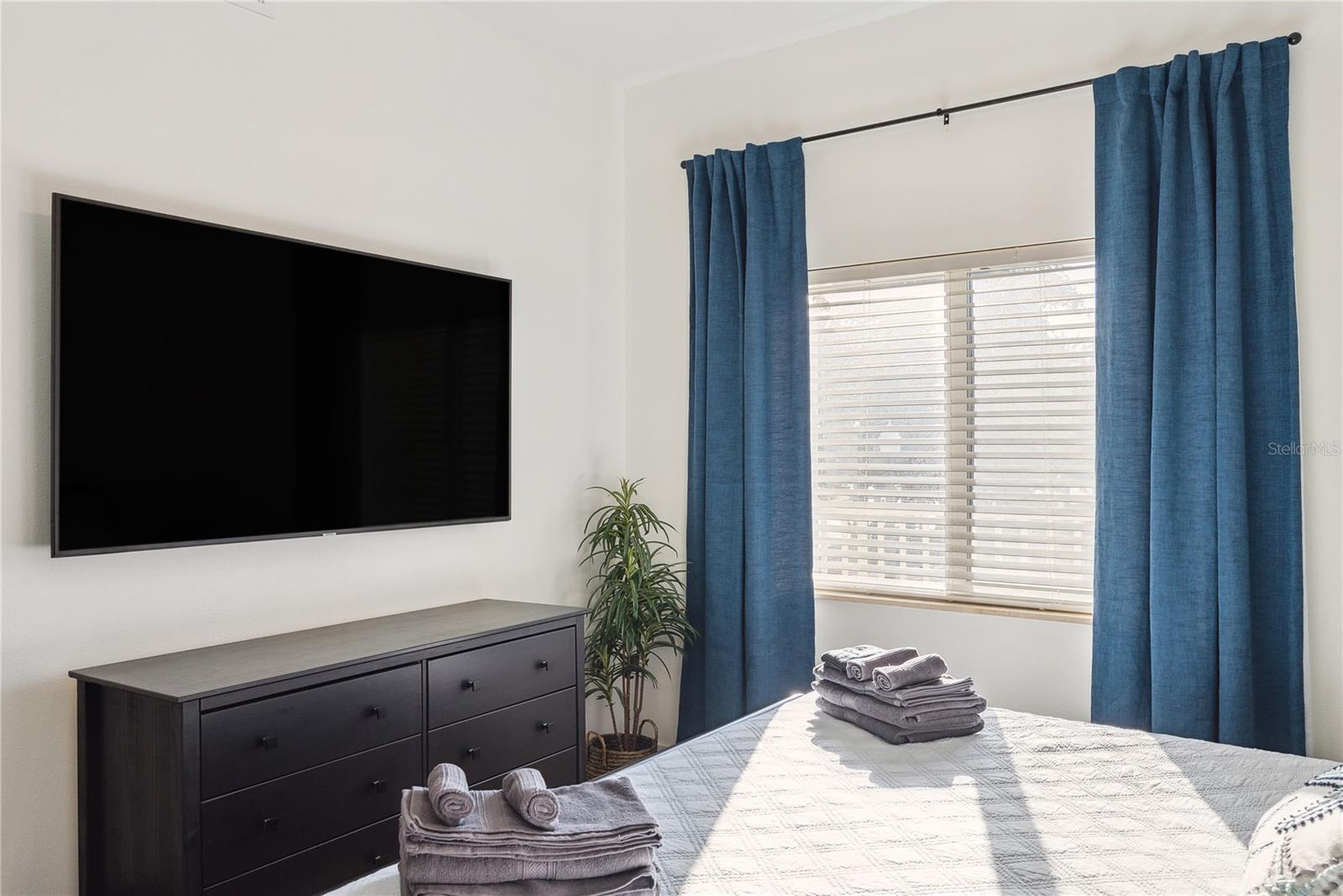 Bedroom with King bed, mounted smart TV, dresser, drapes and decor included