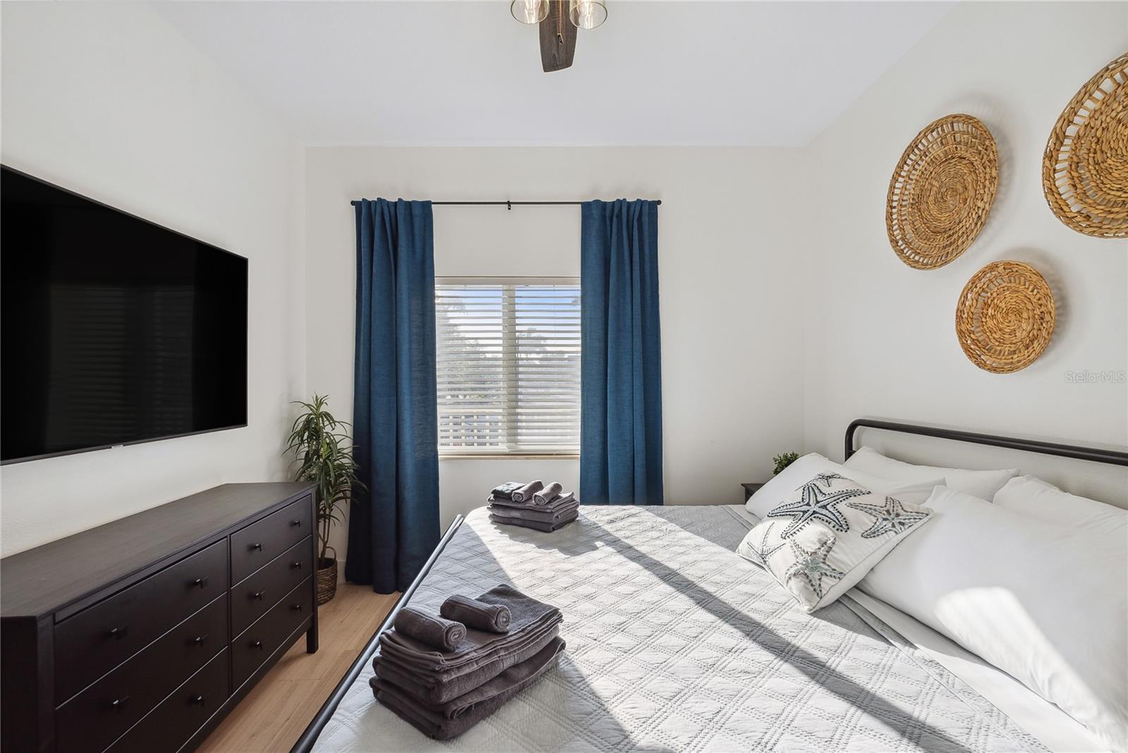 Bedroom with ceiling fan, King bed, mounted smart TV, dresser, drapes and decor included