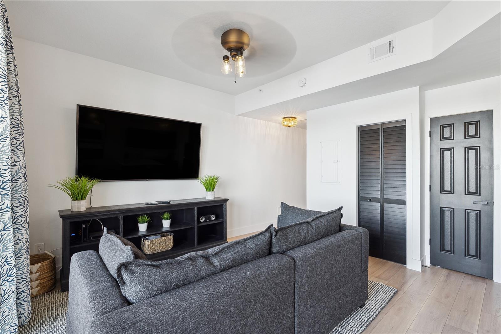 View of Living room with Leather pull-out sleeper sofa, mounted smart TV and storage cabinet, luxury vinyl flooring throughout and custom blackout temperature reducing drapes