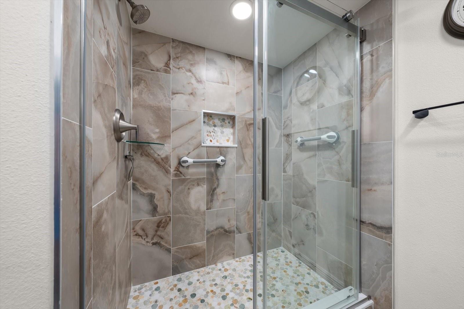 Guest bathroom featuring custom-designed tile work, removable safety grab bars, and a glass shower door.