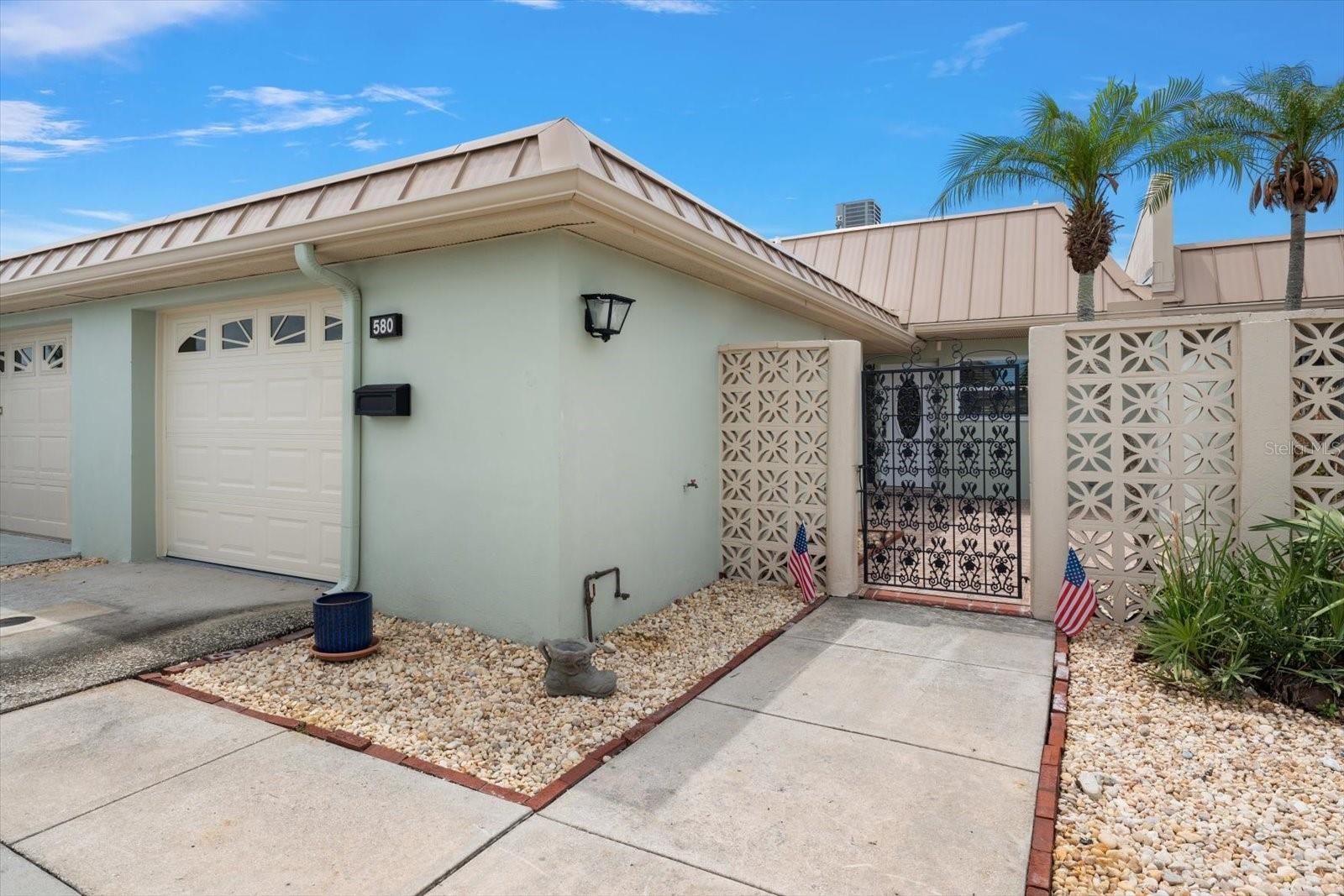 Front entrance featuring a gated patio and beautifully landscaped palm trees.