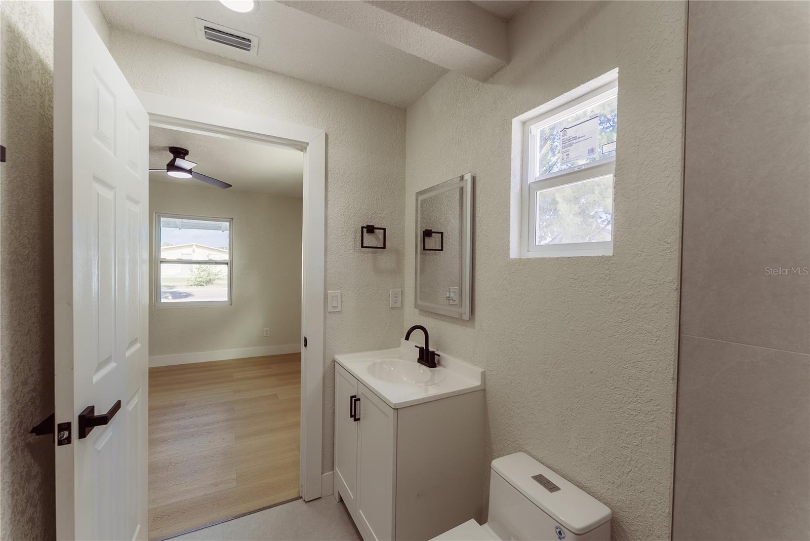 The brand new en suite bath features a white shaker vanity, matte black fixtures, and a framed mirror — with a natural light impact window and direct access to the primary bedroom.