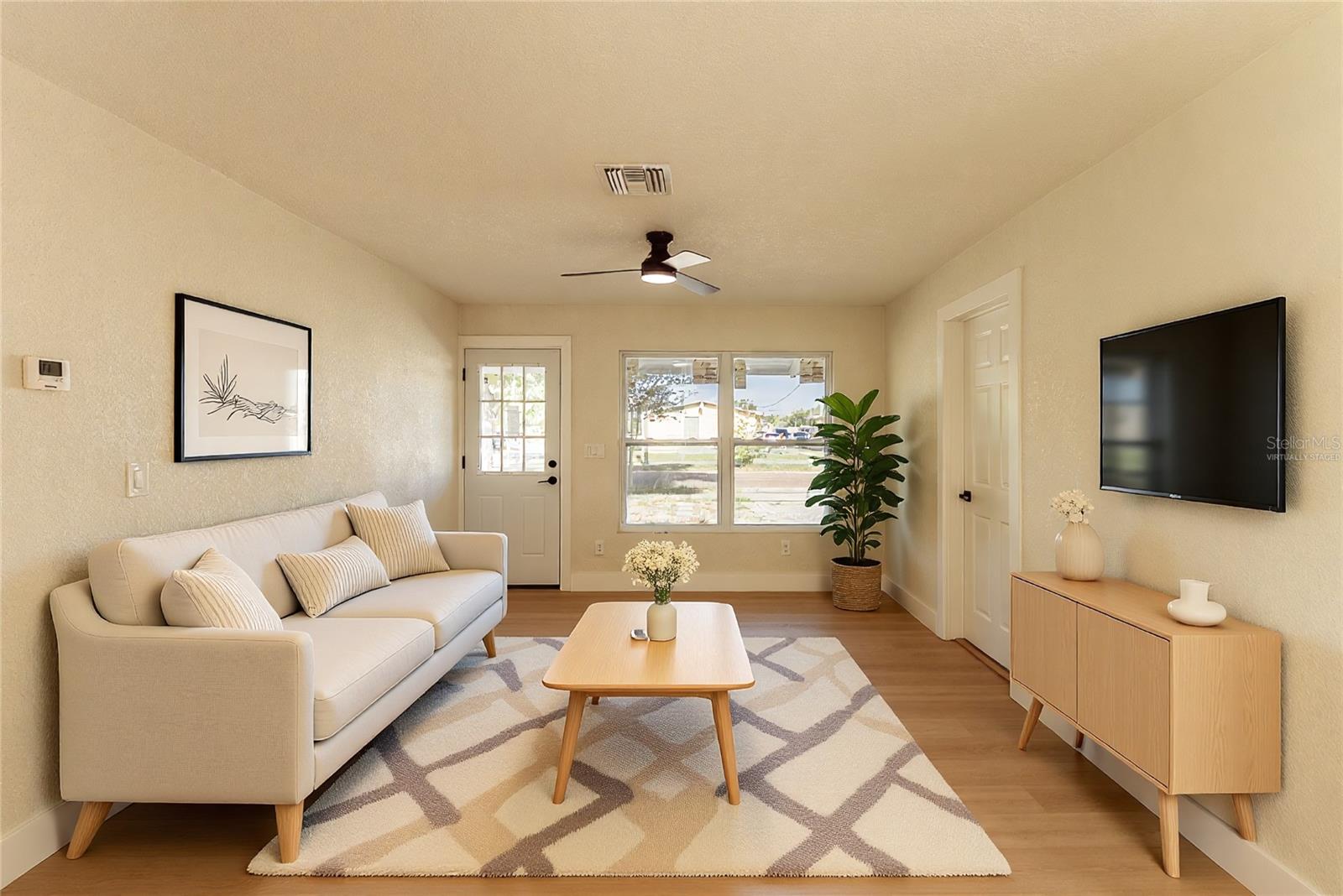 The bright and airy living area welcomes you the moment you step inside, featuring warm luxury vinyl flooring, a modern ceiling fan, and an abundance of natural light pouring through the new windows. The open layout offers flexible living and entertaining space with a clean, neutral palette ready for your personal touch. (Virtually Staged.)