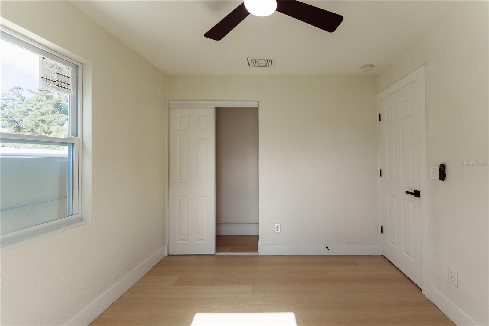 The third bedroom features warm luxury vinyl flooring, a modern ceiling fan, new impact window, and a sliding closet — bright, clean, and move-in ready.