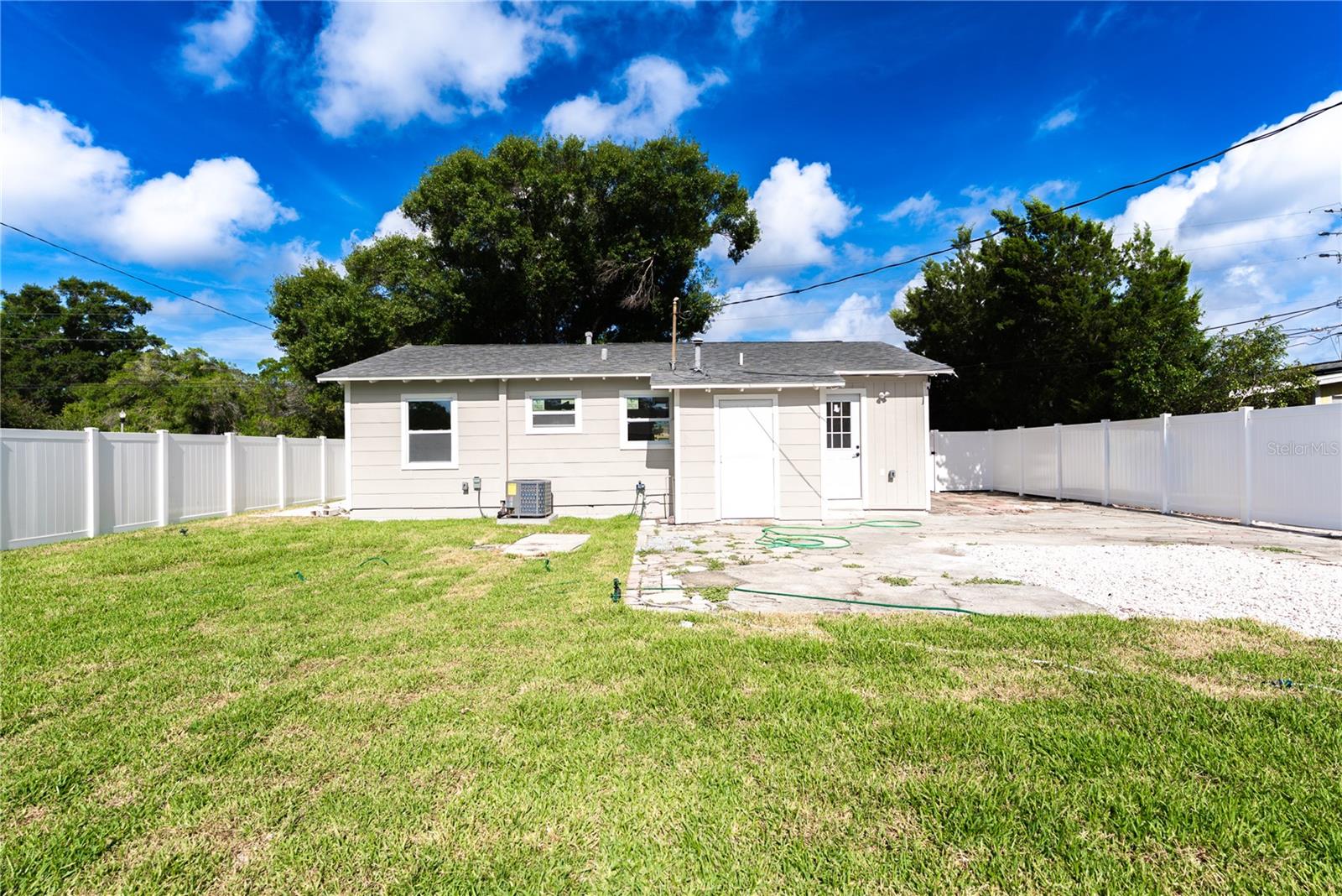 The rear exterior showcases the home's updated back facade, new central A/C unit, and a generous fully fenced yard with new sod, fresh white gravel landscaping, and a gated entry — perfect for entertaining or simply enjoying the Florida sunshine.