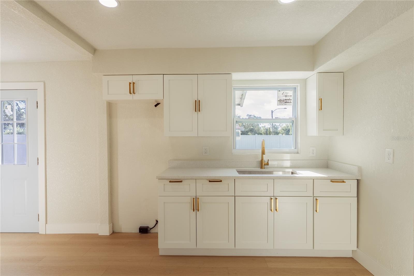The brand new kitchen features crisp white shaker cabinetry, gleaming gold hardware, quartz countertops, and a deep undermount sink with a gold faucet. Recessed lighting and a sunny window complete the space. An appliance package including refrigerator, oven, range, and microwave will be installed prior to closing.