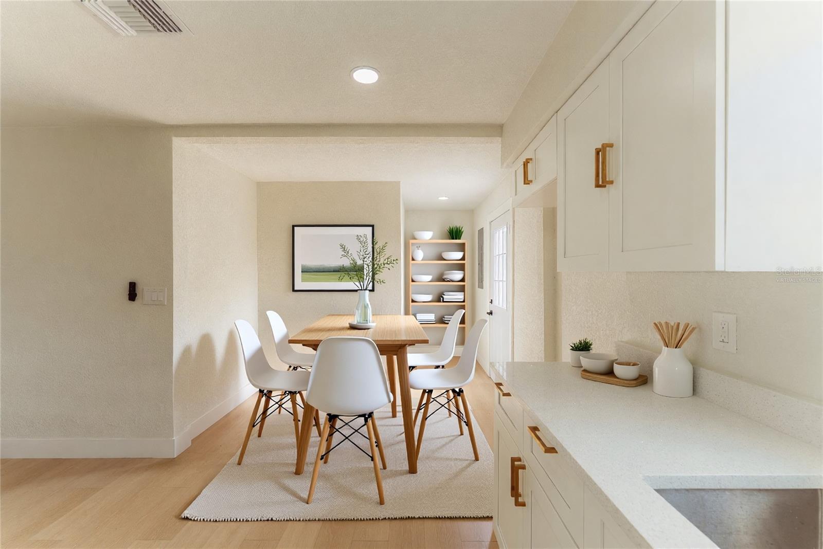 The dining area flows naturally off the kitchen, offering a bright and airy space for everyday meals or entertaining guests. White shaker cabinetry with gold hardware and quartz countertops frame the space, while warm luxury vinyl flooring and recessed lighting carry throughout. A rear door provides convenient backyard access just steps away. (Virtually Staged.)