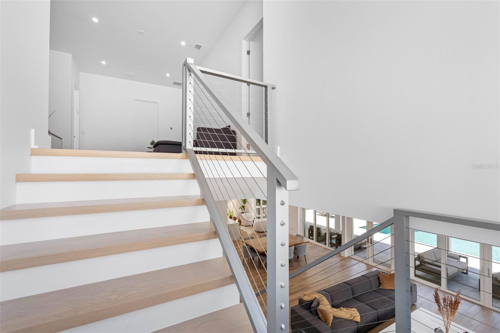 The staircase to the second floor boasts solid wood treads and sleek cable railings, enhancing the minimalist design of the home.