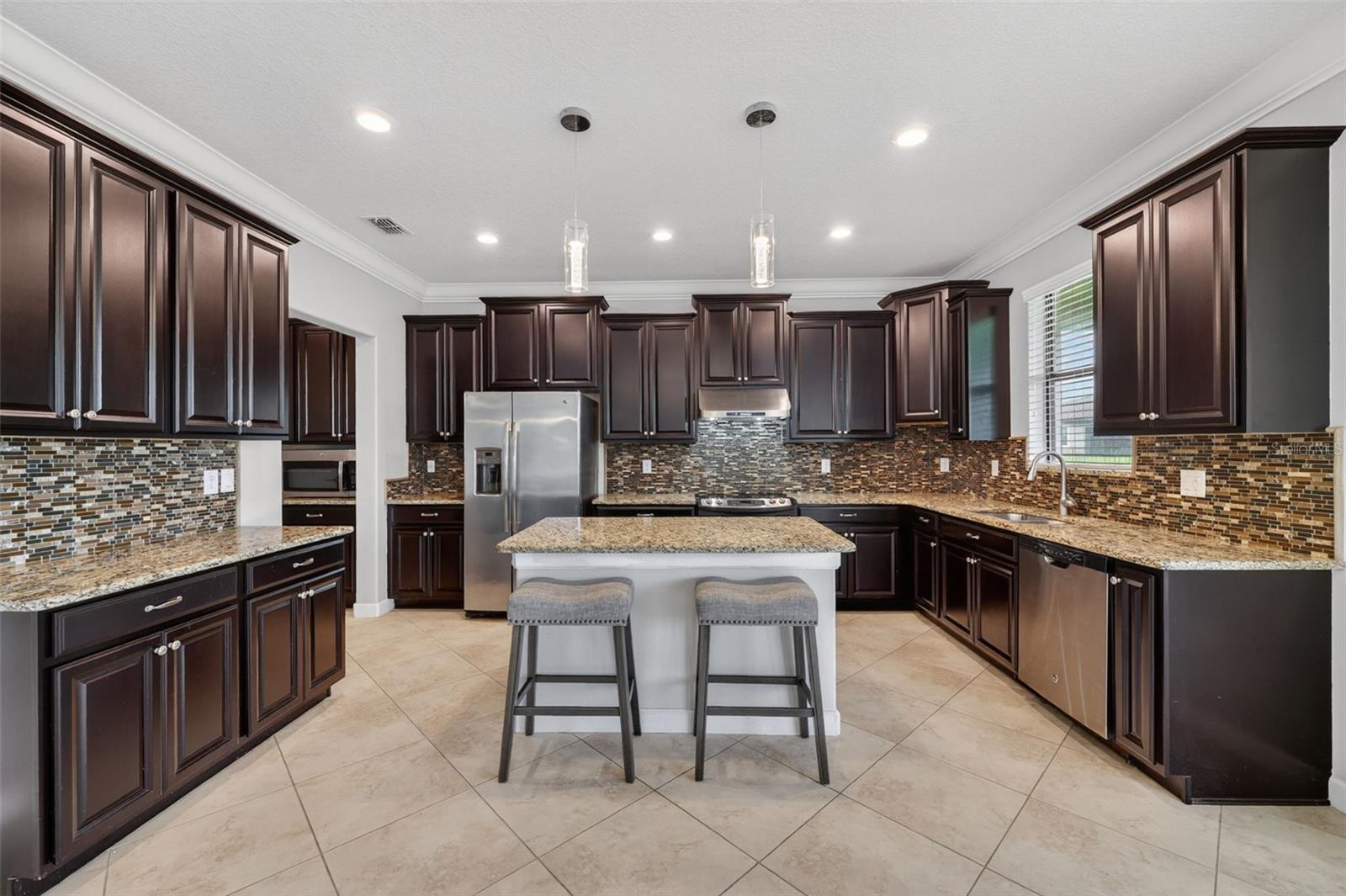 Full Gourmet Kitchen with Crown Molding, Island, Pendant & Recessed Lighting, Abundant Cabinets with Crown Trim, Granite Countertops, Backsplash, GE Stainless Steel Appliance Package, Hood, Window overlooking Serene Pond and Access to Butler's Pantry and Pantry Closet.