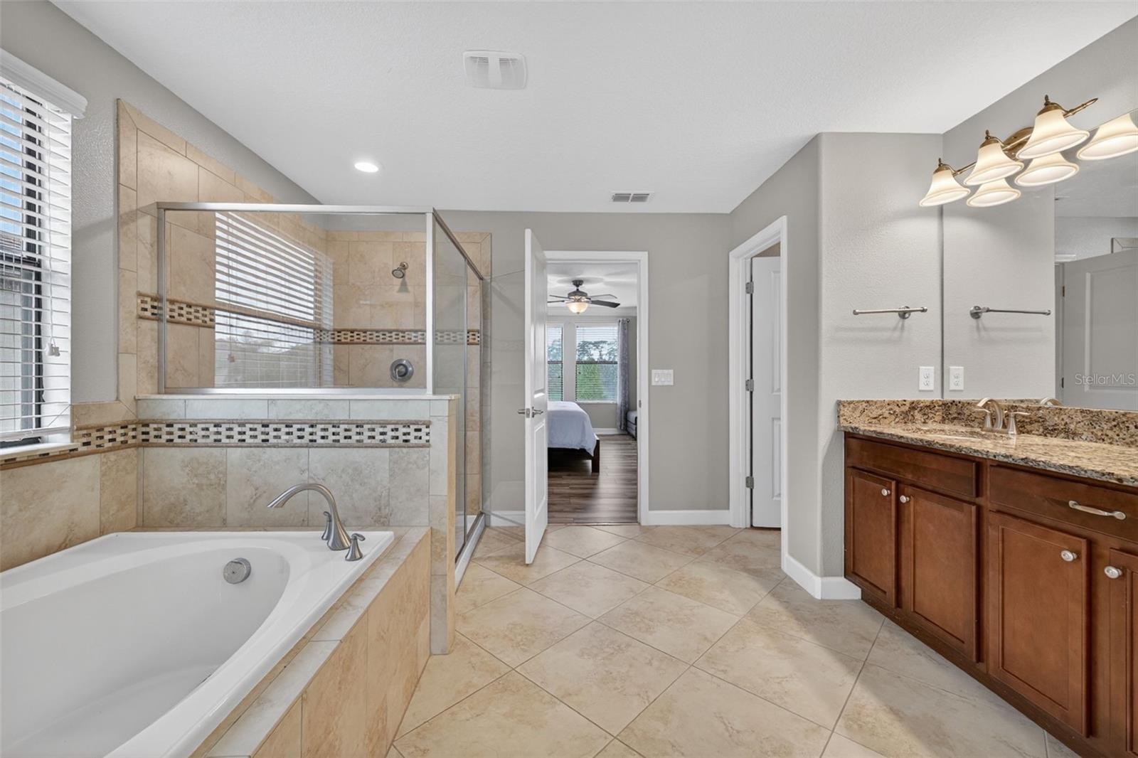 Primary En-Suite Bathroom with Dual Vanities, Granite Countertops, Garden Soaking Tub with Window, Shower Stall with Glass Frame, Private Water Closet, Linen Closet, and Entry to Custom Walk-In Closet.