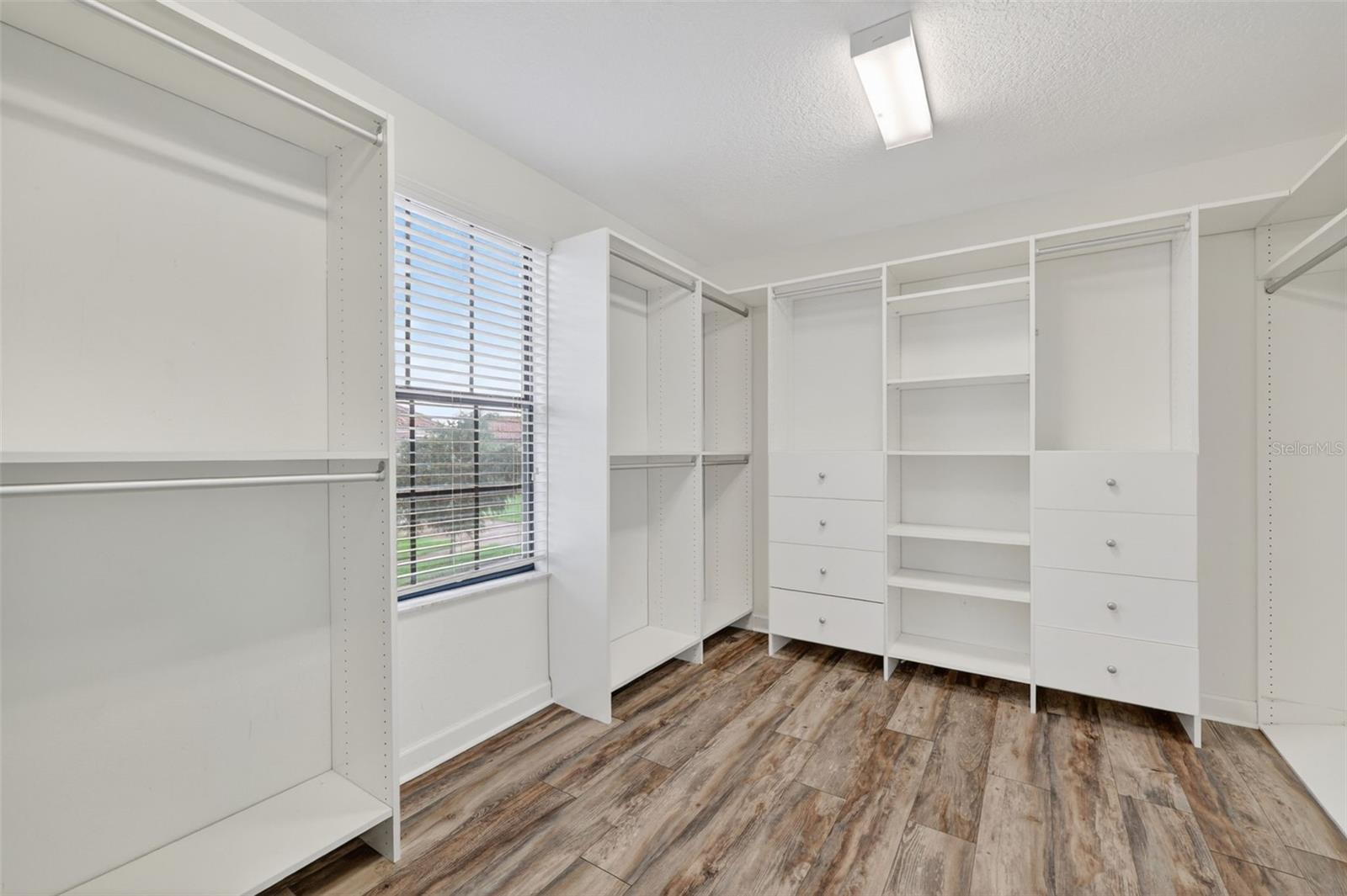 Primary Expansive Walk-In Closet with LVP Flooring, Window for Natural Light, Custom Cabinets, Drawers, Shelving and Storage.