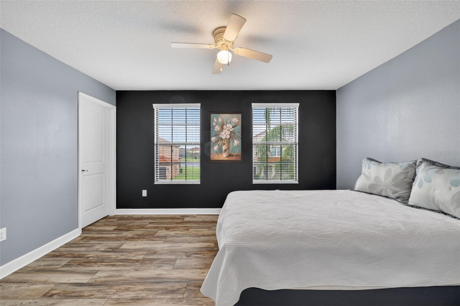 Bedroom #2 with LVP Flooring, Ceiling Fan, Walk-In Closet, Accent Wall, and Windows Overlooking the Front of the Home.