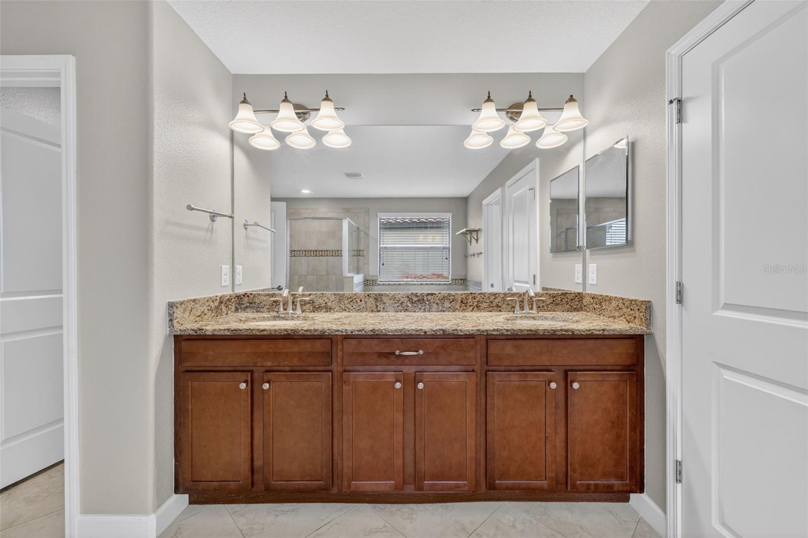 Primary En-Suite Bathroom with Dual Vanities, Granite Countertops, Garden Soaking Tub with Window, Shower Stall with Glass Frame, Private Water Closet, Linen Closet, and Entry to Custom Walk-In Closet.