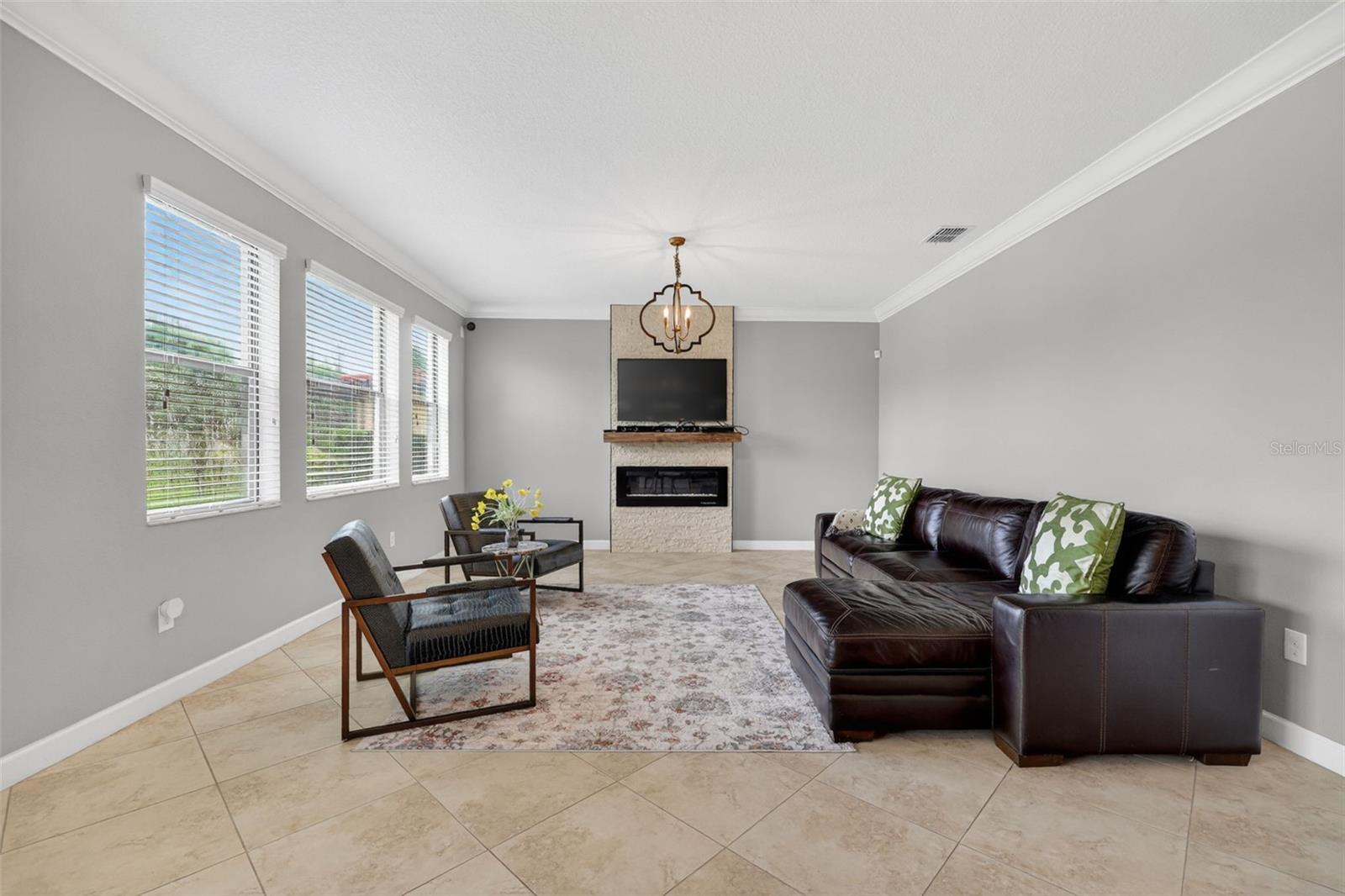 Living Room with Crown Molding, 3 Stunning Windows, Accent Wall with Stone Accent and Chandelier.