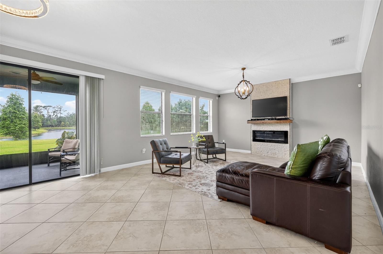 View of Double Sliding Glass Doors and Living Room with Crown Molding, 3 Stunning Windows, Accent Wall with Stone Accent and Chandelier.
