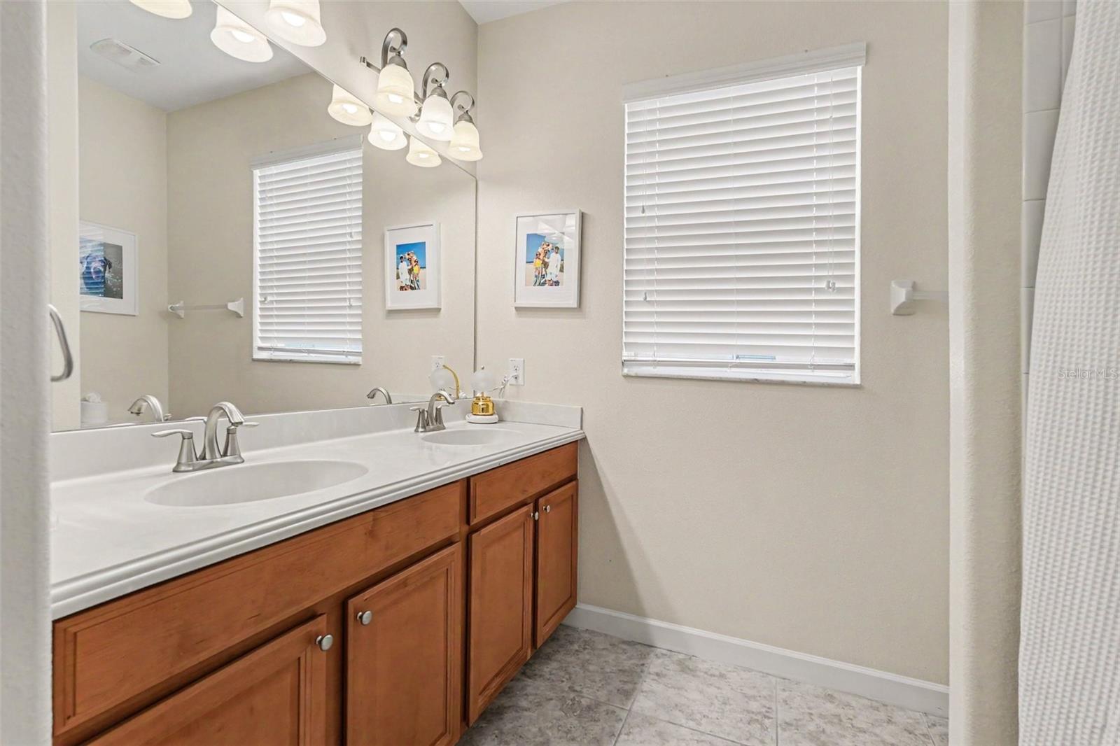 Hall full bathroom with double vanity, wood cabinetry, large mirror in Tampa FL 33647. Sits in between bedroom three and four.