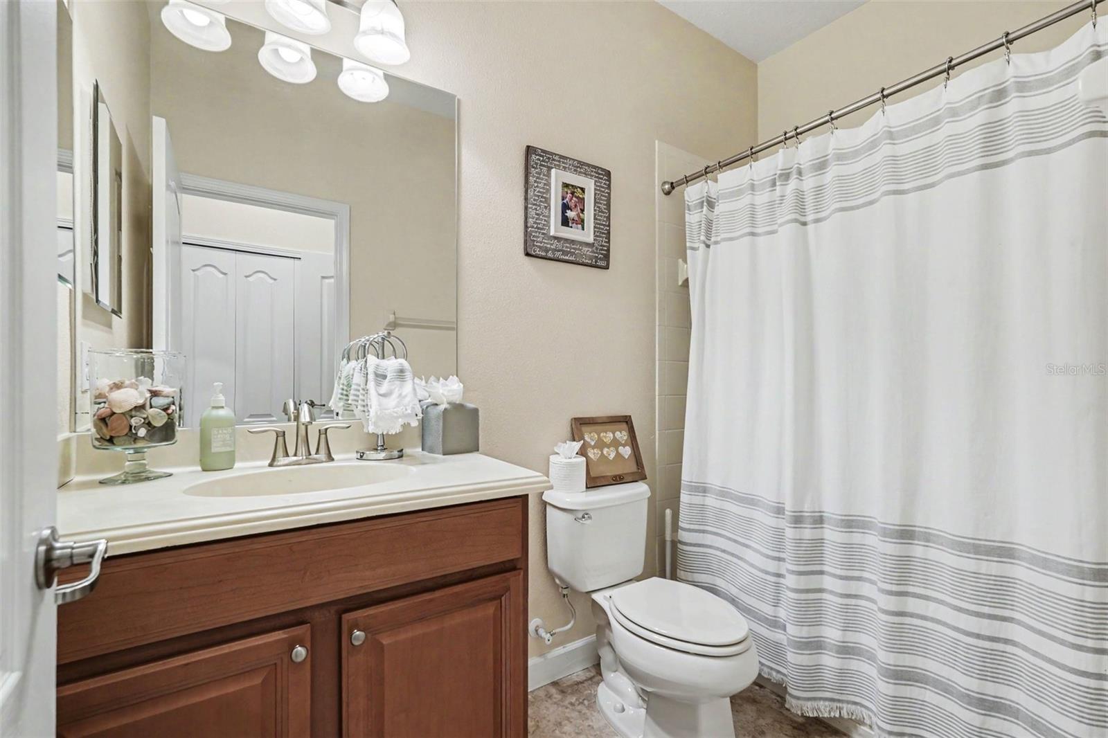 Junior suite (via pocket door access)  full bathroom with single vanity, wood cabinetry, large mirror, tub and shower combo in Tampa FL 33647.