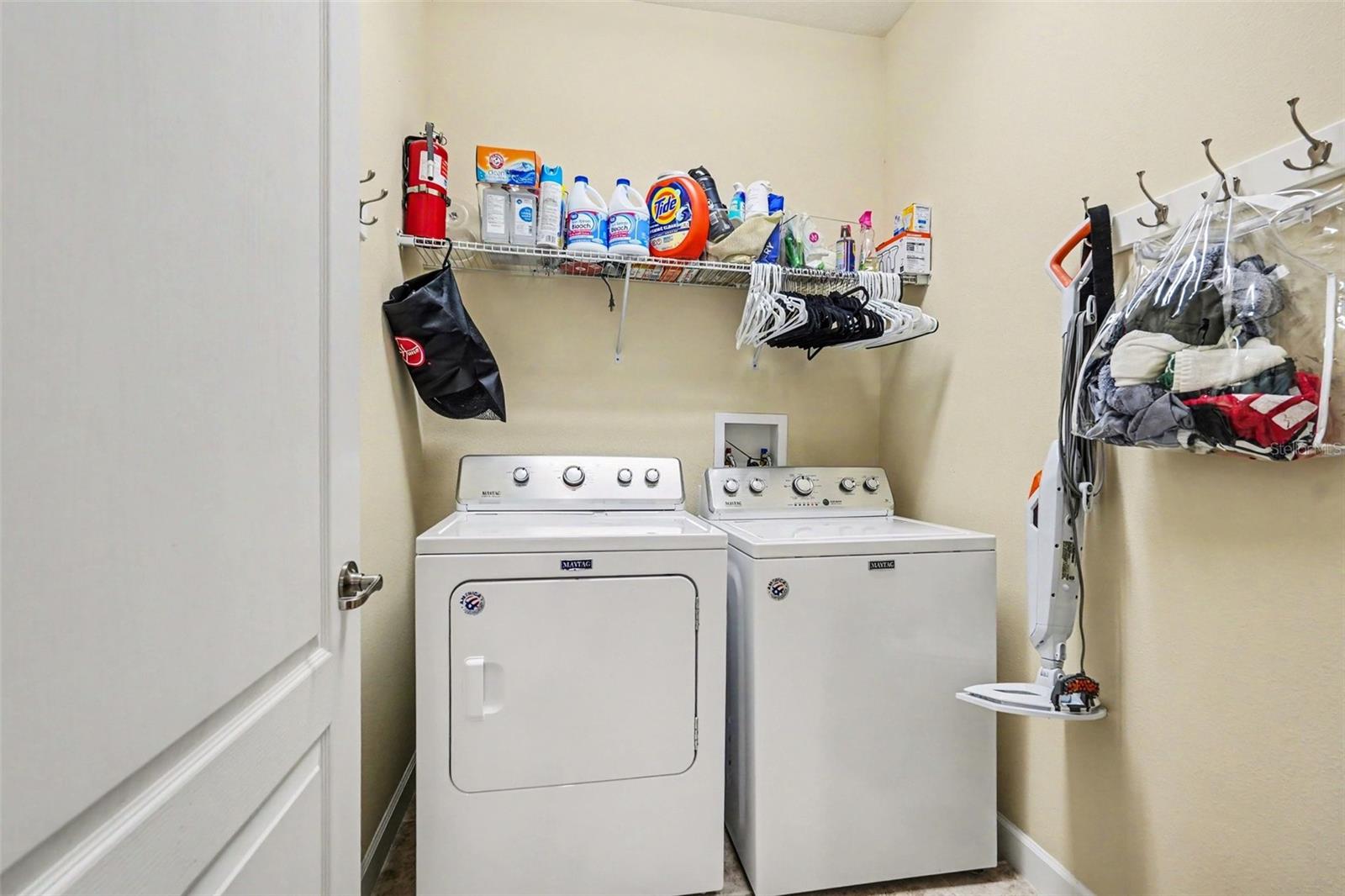 Indoor laundry room with full-size washer and dryer, wire shelving above, and wall hooks for storage in Tampa FL 33647