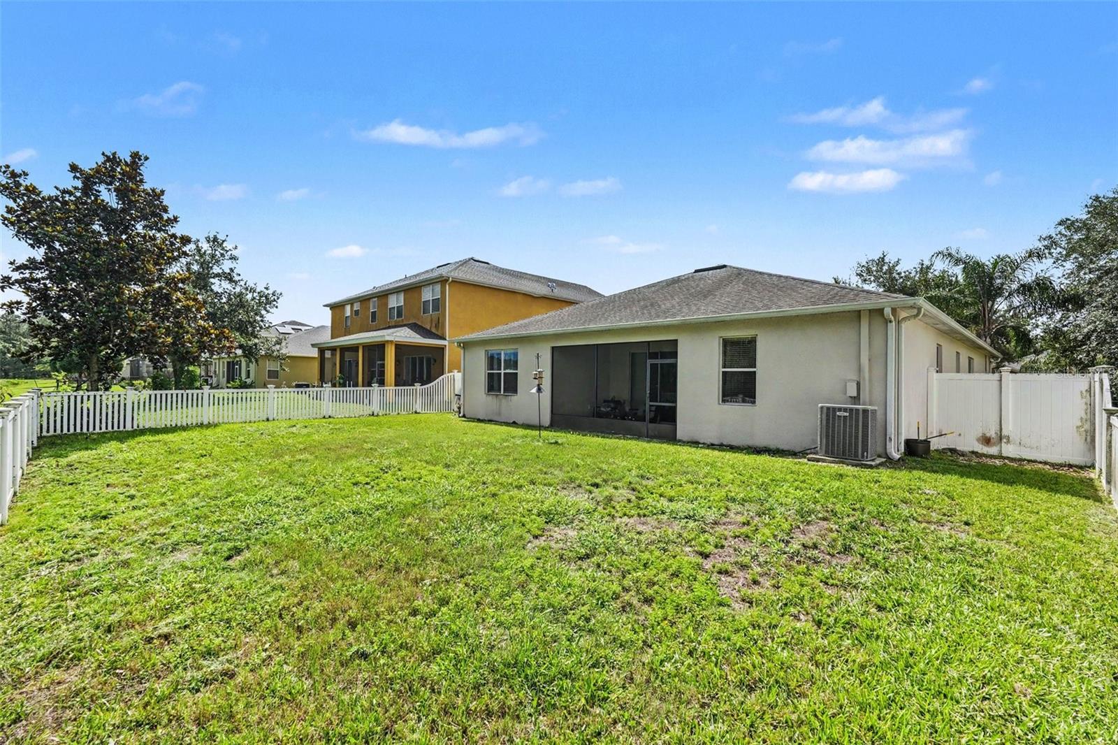Rear exterior wide view showing full fenced yard, white vinyl fence, screened lanai enclosure, and AC unit in Tampa FL 33647