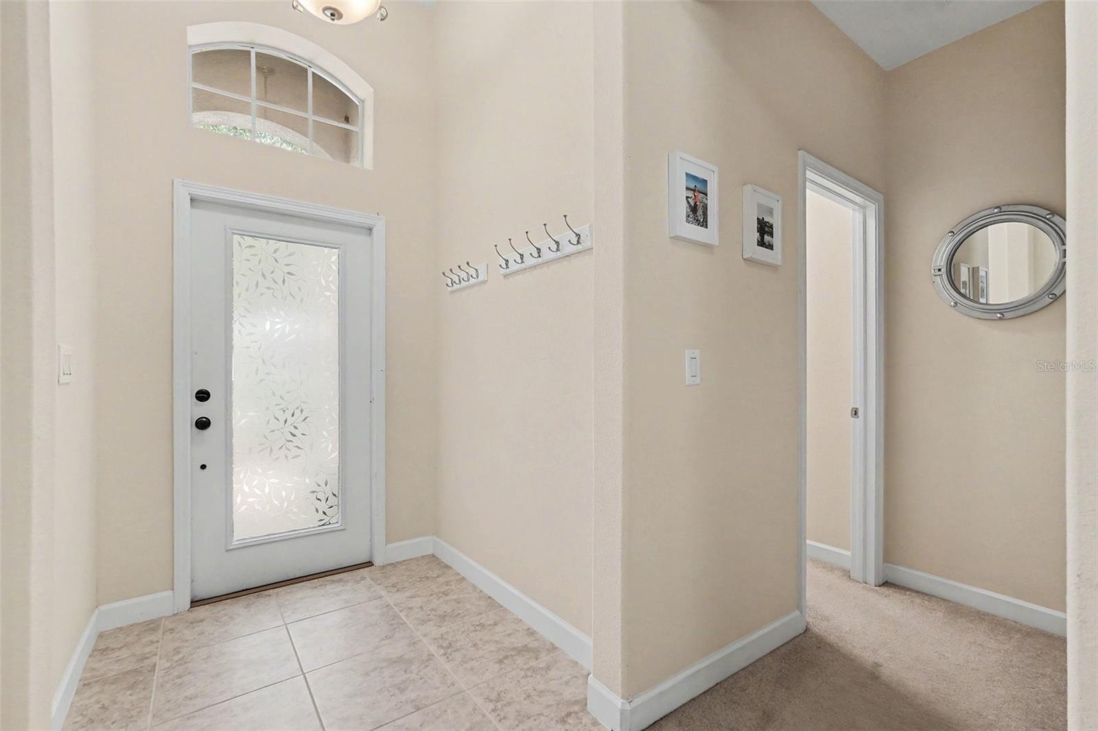Interior foyer with etched glass front door, arched transom window above, tile flooring, junior suite to the right in Tampa FL 33647