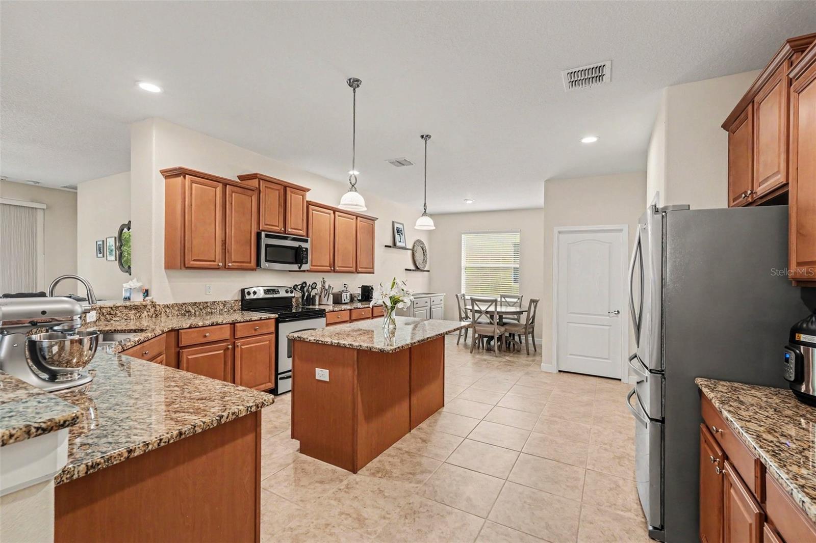 Large kitchen with granite island, full stainless appliance suite, pendant lights, and open view to breakfast nook and dining area in Tampa FL 33647. Laundry room door visible. Pantry and garage to the far right (not visible)