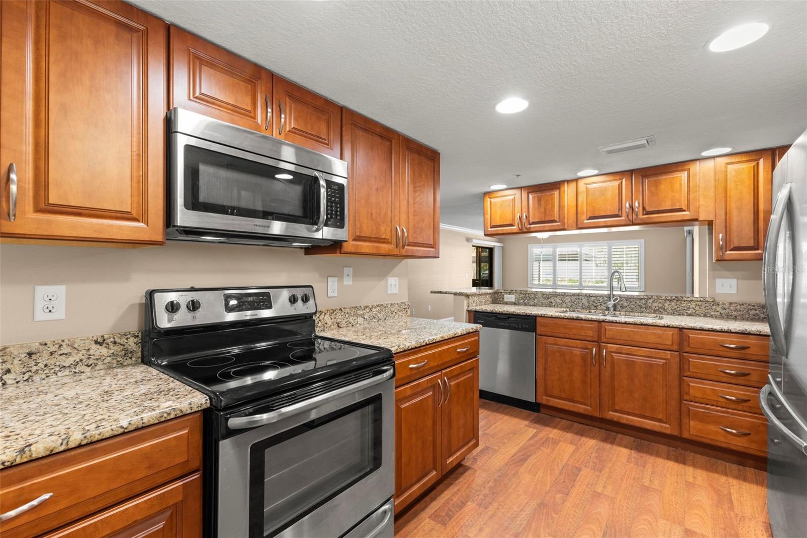 The kitchen features granite countertops, extensive wood cabinetry, stainless steel appliances, wood-look flooring, and generous counter space for meal prep.
