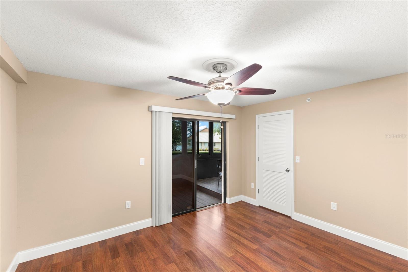 Spacious second bedroom featuring wood-look flooring, a ceiling fan, walk-in closet, and access to the screened lanai.