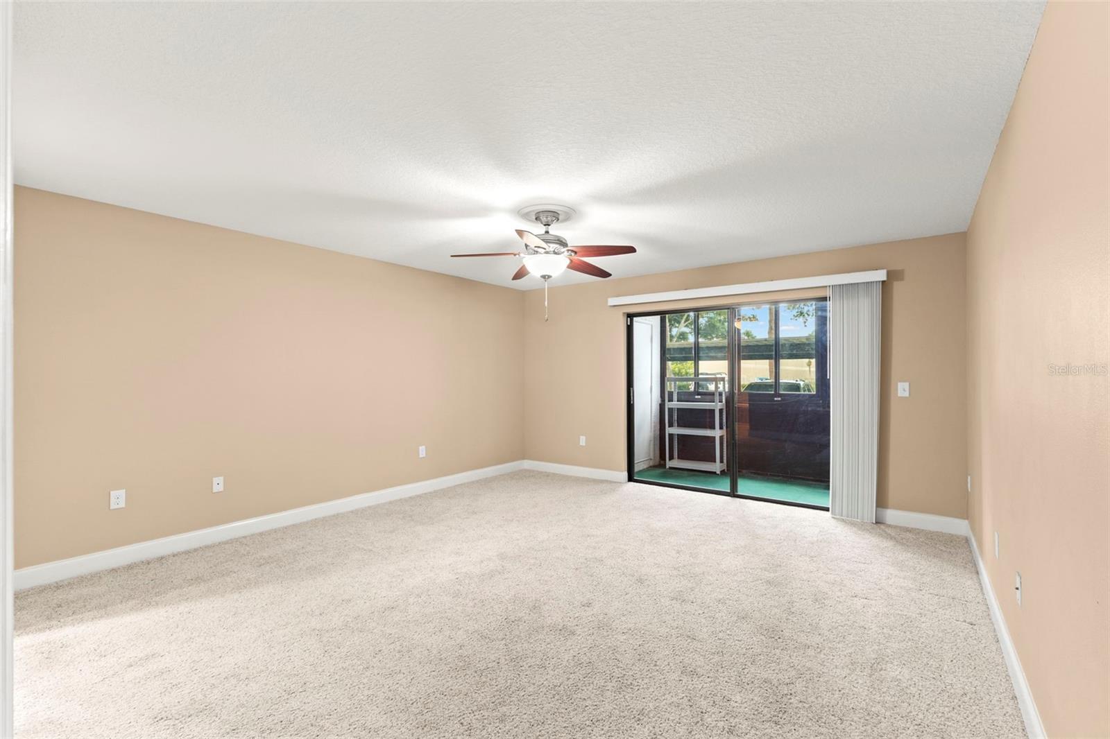 Spacious primary suite with neutral carpeting, ceiling fan, and direct access to the enclosed lanai.