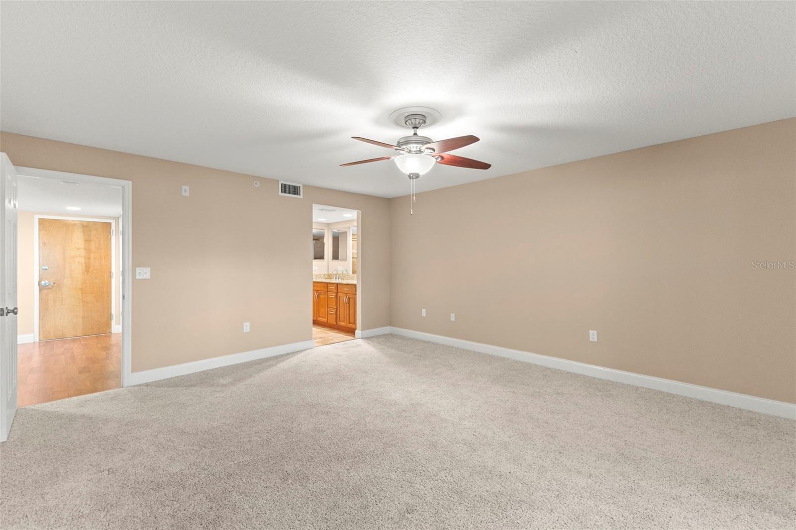 Plush carpeting, a ceiling fan, and a neutral color palette create a comfortable primary retreat with an ensuite bath and walk-in closet.