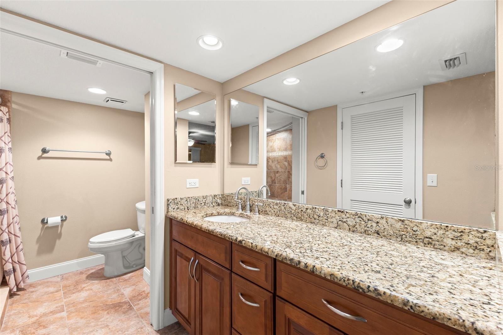 The ensuite bath features a granite-topped vanity, wood cabinetry, recessed lighting, and generous counter space.