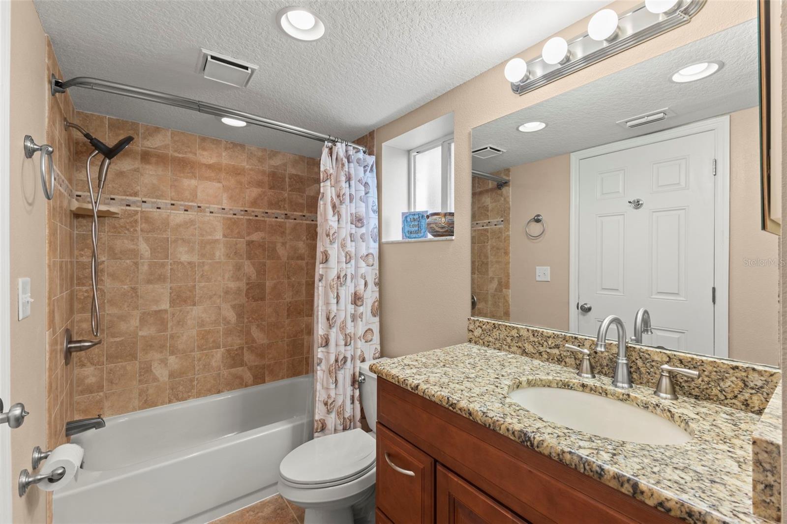 The guest bath offers a granite-topped vanity, recessed lighting, and a tub/shower combination with floor-to-ceiling tile and decorative accent trim.