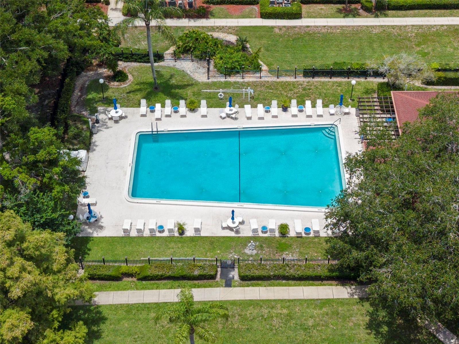 Resort-style community pool surrounded by lush landscaping, ample lounge seating, and sun-drenched deck space.