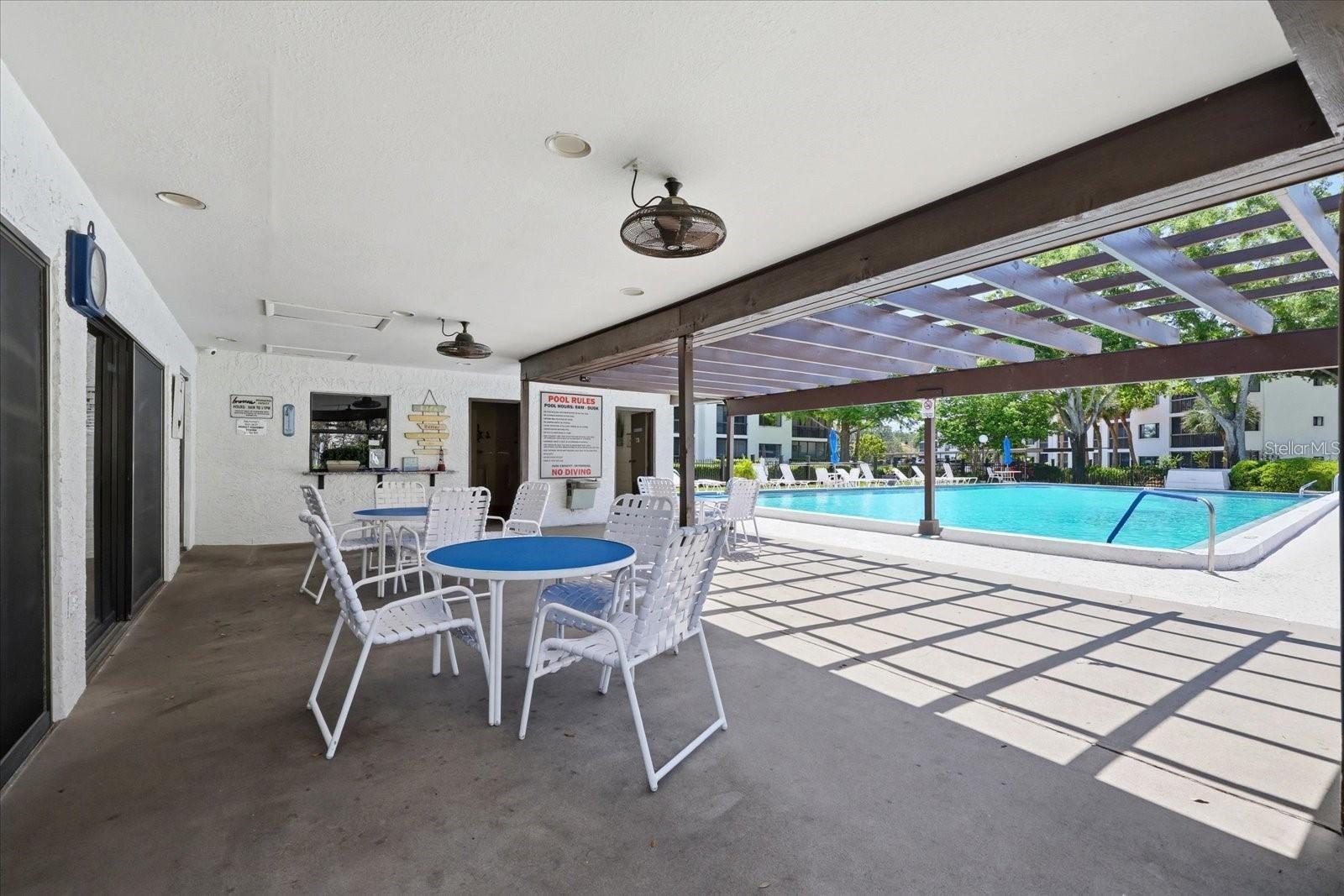 Covered poolside patio offers shaded seating, outdoor dining space, and easy access to the community pool.