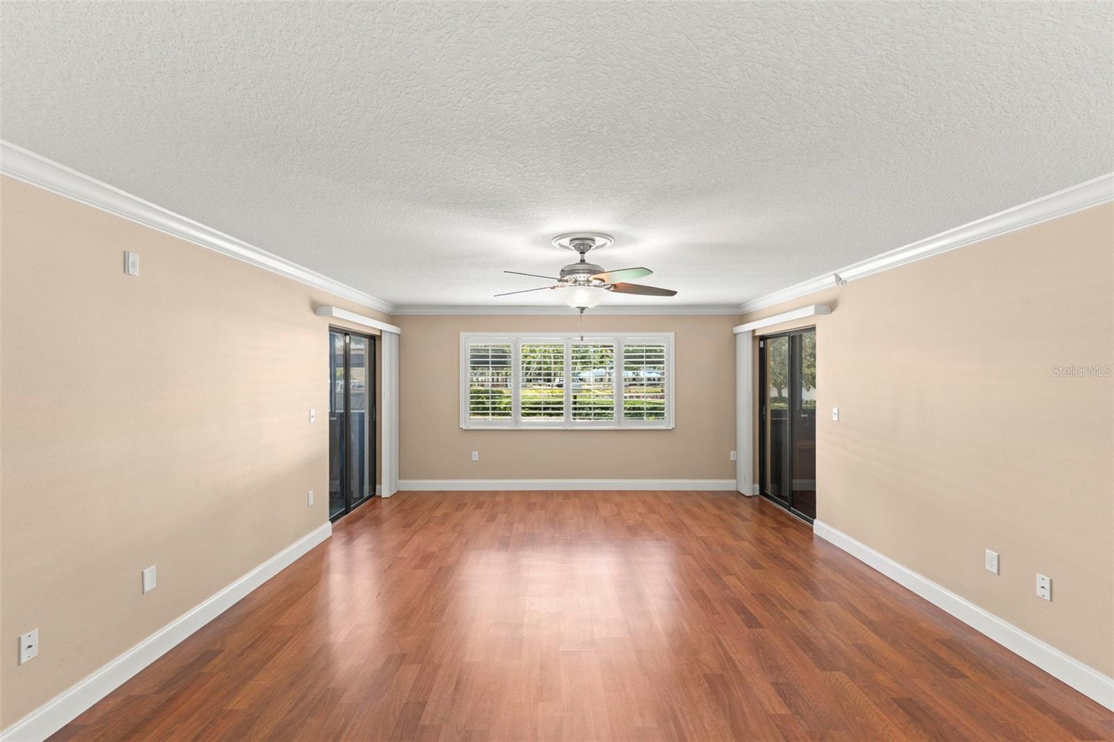 The spacious living room features crown molding, plantation shutters, wood-look flooring, and access to two enclosed porches that expand the home's living space.